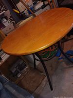 Round wooden table with two folding edges and tripod metal legs shown from an angled side view, surface and support legs visible.
