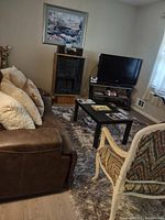 Black metal TV stand with three glass shelves in a living room setting. The stand supports a flat-screen television and has media devices on the lower shelves.