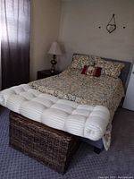 Wicker chest seat with storage placed at foot of bed, showing cushion and woven wicker design
