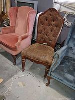 Photo showing a pink wingback chair along with two other chairs, highlighting the chair's fabric and wooden legs.
