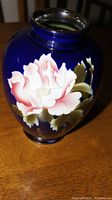 Close-up of the front of the jar showing the detailed pink and white flower with green leaves on a cobalt blue background.