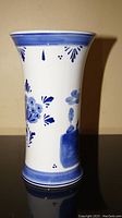 Side view of tapered blue and white vase with floral and leaf painted details.