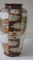 Full side view of the vase showing intricate block patterns in brown, orange, black, and white with gold accents.