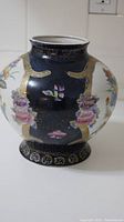 Front view of the decorative jar showing black and white panels with floral and gold accent paintings.