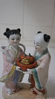 View of porcelain figurine showing both children and tray with fruit and small gold object