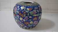 Side view of round ceramic jar with intricate floral pattern on blue background.