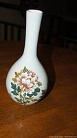 Full view of white porcelain vase with painted pink and white peony flower motifs and green leaves on bulbous base with narrow neck.