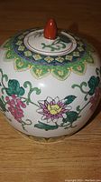 Side view of the ceramic grape jar showing floral and grapevine hand-painted design and the ornate border near the top edge.