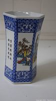 Hexagonal porcelain vase showing blue and white floral borders and a painted panel with a woman in traditional Chinese attire and calligraphy.