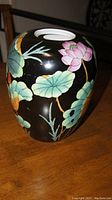 Front and side view of ceramic lotus jar showing painted lotus flowers and leaves on black background.