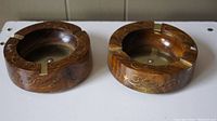 Two circular wooden ashtrays with gold swirling inlay designs and three cigar rests shown from the top view.
