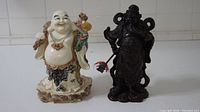Pair of Asian figurine statues, Buddha and warrior, shown side by side on white tiled background.