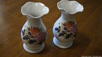 Pair of floral porcelain jars shown from the top angle on a brown wooden surface, showcasing the scalloped rim and colorful floral design.