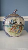 Front side of the pumpkin-shaped ceramic jar showing seated Asian ladies in traditional dress near water and pagoda.