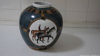 Side view showing the rider horsemen illustration on the decorative jar with contrasting blue and brown glaze.