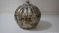 Front view of a round ceramic jar with lid featuring gold floral patterns and scalloped edges.
