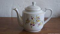 Front view of the white ceramic teapot showing the floral design and curved spout.