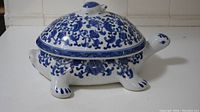 Full side view of ceramic turtle jar with lid showcasing blue floral patterns and shape