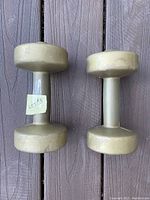 Two gold-colored dumbbells placed side by side on wood surface, showing shape and condition.