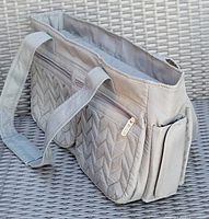 Grey LUGG handbag side and front view showing double handles, two large zippered front pockets with chevron quilted design, main zippered compartment, and side phone slot pocket.