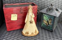 Photo of set with red flower pot, angel figurine, and butterfly candle lantern on wicker background.