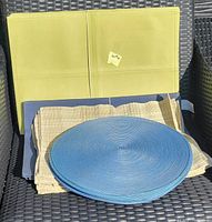 Yellow leather, beige cloth, and round blue cloth and wicker placemats arranged on a dark chair outdoors.