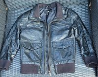 Black leather children's jacket laid flat with front facing up. Shows ribbed cuffs, collar, hem and multiple pockets.