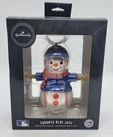 Front view of the Hallmark Blue Jays snowman Christmas ornament in its original packaging showing the snowman dressed in Blue Jays baseball attire holding a bat.