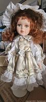 Porcelain doll with red curly hair in cream lace dress and matching bonnet