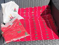 Red Christmas placemats laid out with red and white embroidered napkins on a black wicker chair.