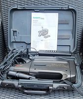 Panasonic Omni Movie VHS recorder with microphone, power cords, and instruction manual inside open carrying case.