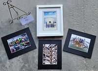 Set of four framed photos and one black metal photo stand displayed on concrete floor.