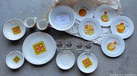 Top-down photo of all dishes and glasses arranged showing Ridgway Ironstone plates and mugs, orange fruit plates, white bowl, and curling glasses.