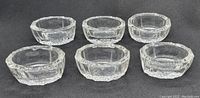 Six vintage clear cut glass salt cellars viewed from the side, showing varying faceted cut glass patterns and overall round shape.