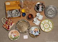Image showing variety of kitchen items including 12 piece escargot set, crystal glasses, decorative plates, metal trays, and kitchen accessories arranged on a surface.