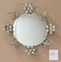 Front view of vintage round mirror with metal floral design frame, displaying scratches and wear on reflective surface.
