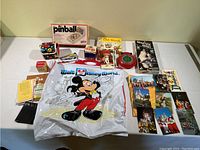 Full lot showing Walt Disney World plastic bag, pinball game, Old Maid game box, Slinky Jr., Master Mind, postcards, and other small booklets and toys.
