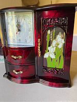 Front view of the jewelry box shows the clock on the left, two drawers beneath, and a floral decorated door on the right.