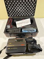 VHS video camera inside a Solidex hard carrying case with foam padding, includes cables and instruction manual.