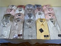 Top view showing full 20 men's dress shirts grouped in four rows, colors include white, pink, beige, yellow, olive green, striped and solid styles. All shirts size 15 1/2, many with original packaging.