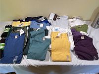 Photo showing a large assortment of knit tops and t-shirts in various colors neatly folded on a table.