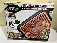 Photo of the Gotham Steel Electric Smoke-less Grill box showing branding, features, and a cooked steak on the grill.