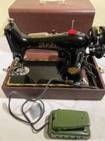 Full view of vintage black BelAir sewing machine on wooden base with power cord and green foot pedal in front. Brown textured carrying case behind.