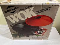Front and top view of the original box for West Bend 6 quart electric wok showing product image, brand, model number and key features like easy-to-clean non-stick surface and red glass lid.