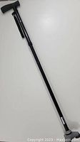 Full length view of the black adjustable Hurrycane cane showing ergonomic handle, wrist strap, and the rubber tip base.
