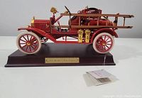 Left side view of the Franklin Mint 1916 Model T Fire Engine collectible showing detailed body, ladders, and gold accents, placed on wood base with plaque.