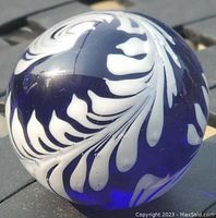 Close-up photo of the cobalt blue glass paperweight showing white feather plume design on one side of the spherical paperweight.