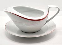 Front side view showing the full profile of the white porcelain gravy boat with red accent line and the matching underplate as base.