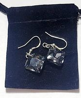 Pair of sterling silver pierced earrings with black faceted square gemstones resting on a black velvet pouch.