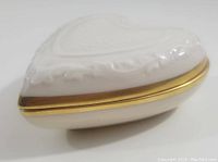 White heart-shaped porcelain dish with embossed heart design and gold trim, viewed from side angle showing depth and lid fit.